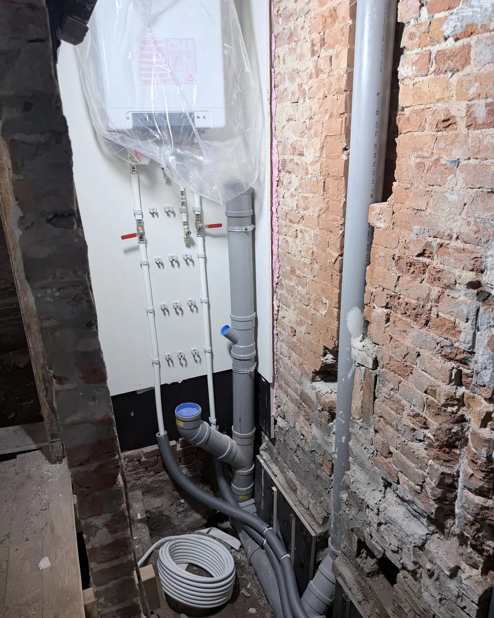 Bouwfoto Newtonstraat 286: nieuwe vloerverdeler, waterleiding en PVC-riool tegen de oude bakstenen muur, vóór de afwerking